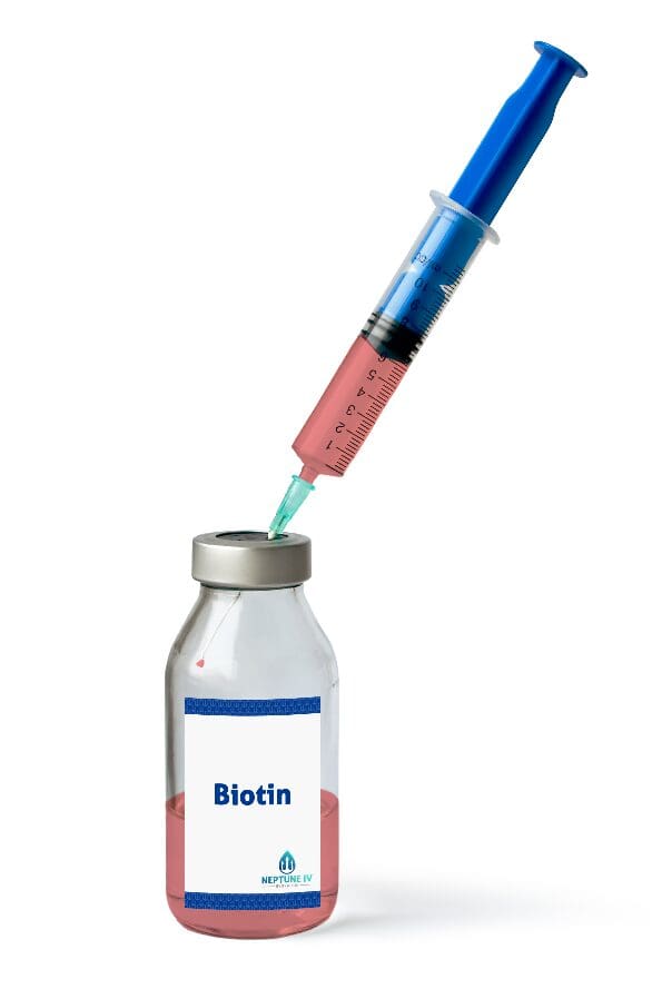 A syringe drawing a liquid from a vial labeled "biotin," part of a mobile iv therapy regimen.
