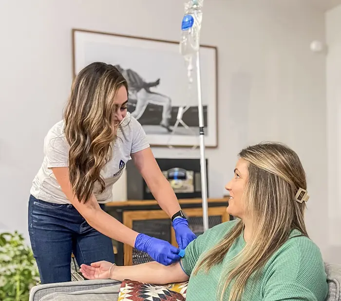 A healthcare professional is administering a mobile iv therapy rich in vitamins to a smiling female patient in a comfortable home setting.